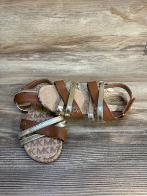 Brown and gold toddler sandals with MK logo, strappy design on wood background