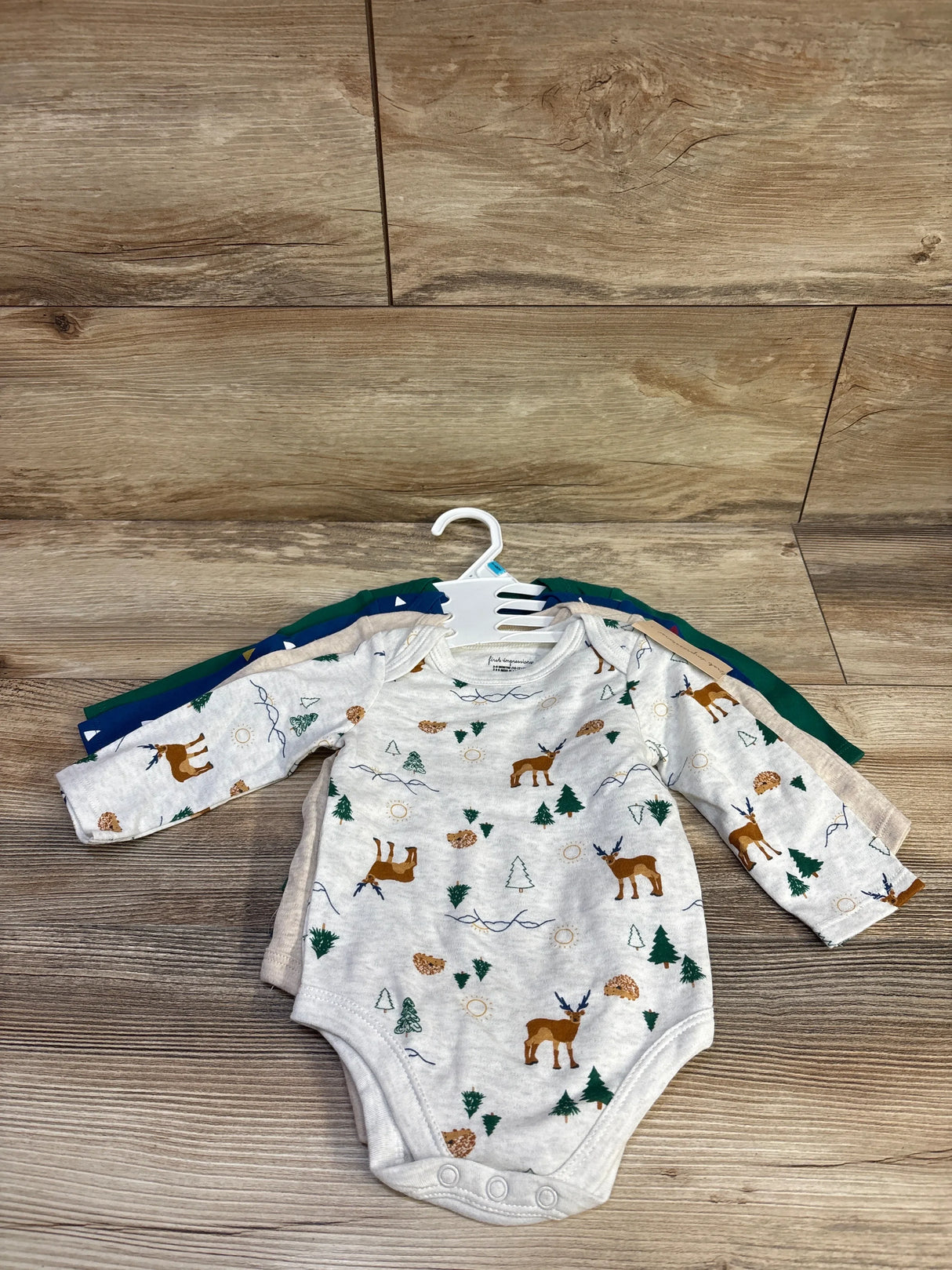 Front view of 4 long-sleeve baby bodysuits, grey deer-print bodysuit on top, snap closures visible, on wood floor background
