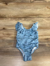 Flat-lay front view of baby blue one-piece swimsuit showcasing beach print and ruffled shoulder straps on wood background