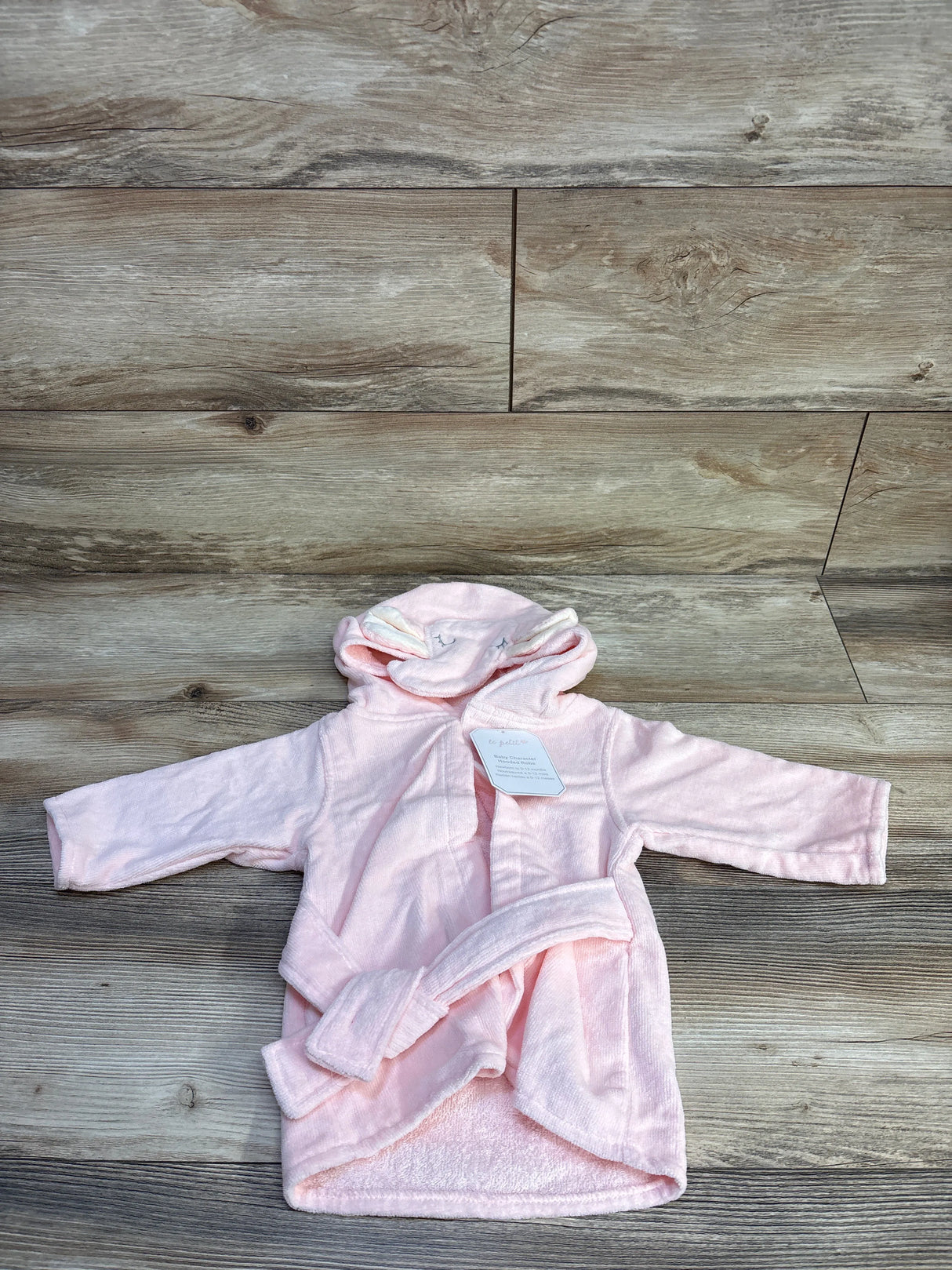 Front view of pink Le Petit Elephant hooded baby bathrobe showcasing attached hood with elephant ears and matching belt on wood floor background