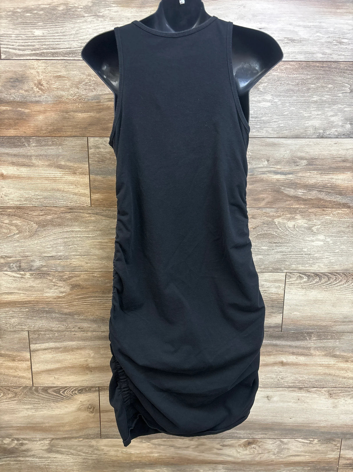Front view of black maternity tank bodycon dress with side ruching and high neckline on a mannequin against wood backdrop
