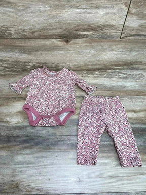 Top view of pink floral two piece baby bodysuit and pants showing ruffled cuffs and snap closure on wood background