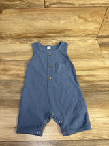 Flat lay of blue ribbed henley shortie romper showing wooden button placket, chest pocket, and snap crotch on wood floor background