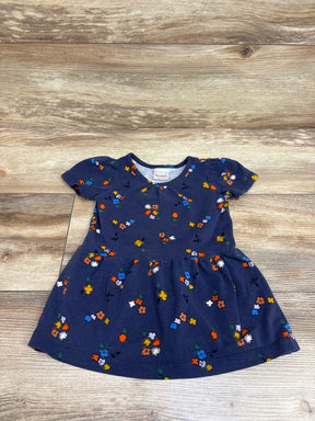 Front view of Hanna Andersson navy floral peplum dress with colorful floral print and gathered skirt on wood background