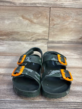 Front view of Cat & Jack Ade footbed sandals (kids size 8C) showcasing green camo pattern, orange buckles, and adjustable straps on wood-look background