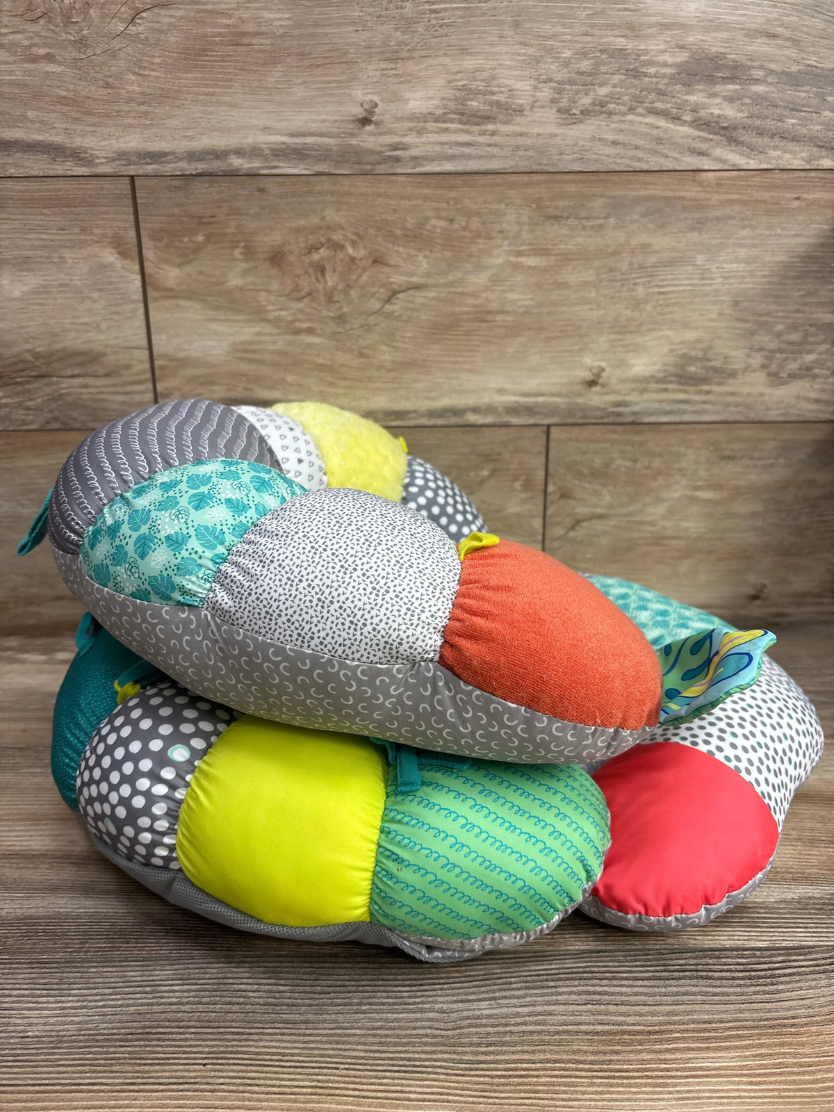 Angled view of Infantino 2-in-1 Tummy Time & Seated Support showcasing colorful patterned padded sections with a wood-look background