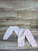 Flat lay of two baby pull-on pants, one solid pink and one pale pink with gray cloud print on wood background