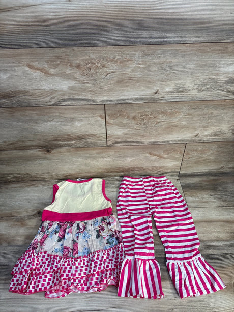 Flat lay of 2-piece girls set showing cream sleeveless floral dress with ruffled hem and pink striped bell-bottom pants on wood floor