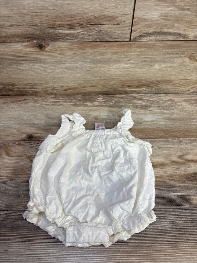 Top view of ivory baby bubble romper with ruffled shoulder straps, jacquard texture, elasticized leg openings on wood floor