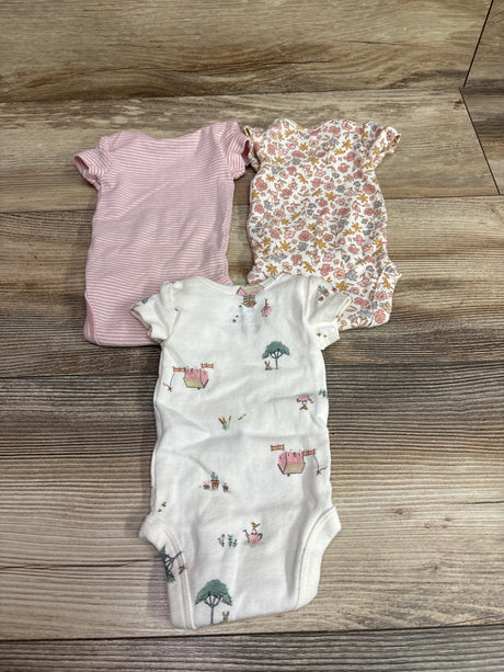 Top view of Carter’s preemie bodysuit three-pack showing pink striped, floral, and illustrated white bodysuits on wood