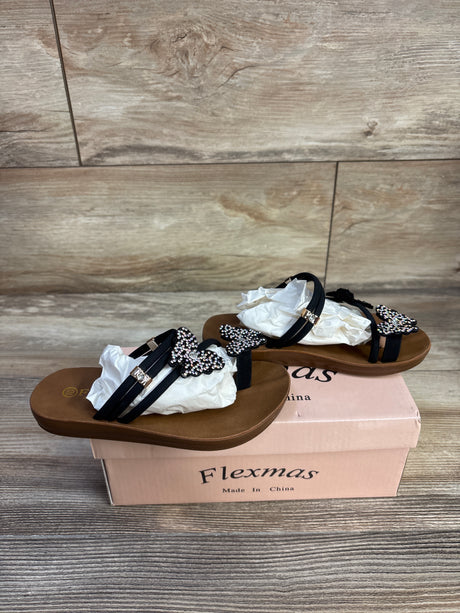 Three quarter view of black Flexmas toddler sandal showcasing rhinestone butterfly straps on a pink shoebox and wood floor