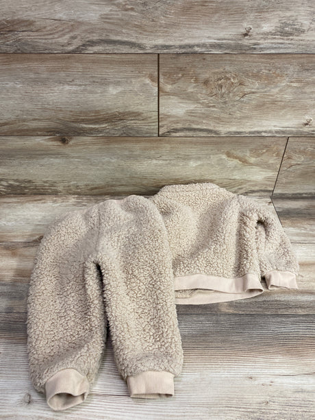 Top-down view of beige sherpa jacket and pants set showcasing textured fleece and ribbed cuffs on a wood floor