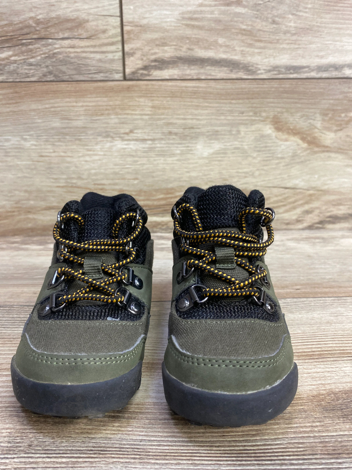 Pair of green and black toddler hiking boots with yellow and black laces on wooden floor