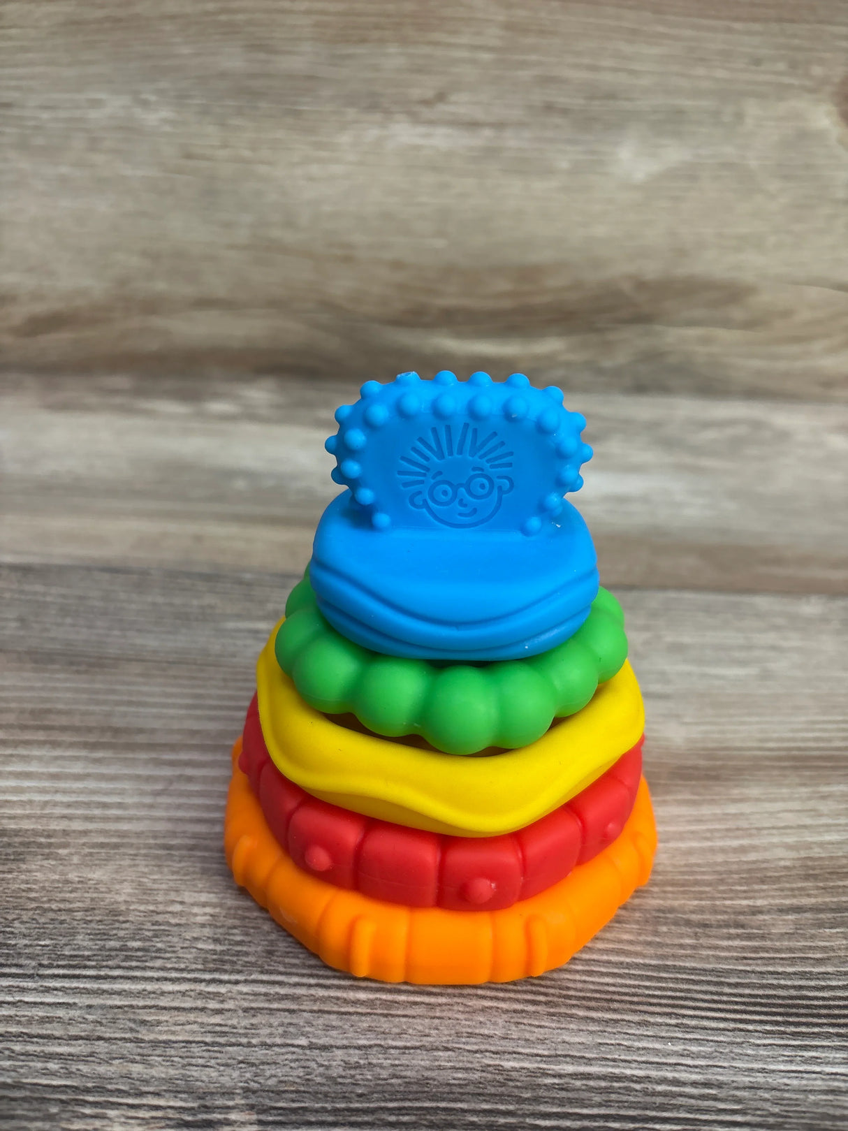 Front view of Baby Einstein 5-piece stacking teether set showing colorful textured rings with blue top on wood surface