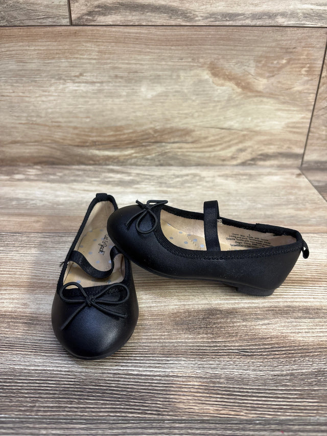 Three-quarter view of Cat & Jack Nora slip-on ballet flats showing front bow and elastic instep strap on light wood background