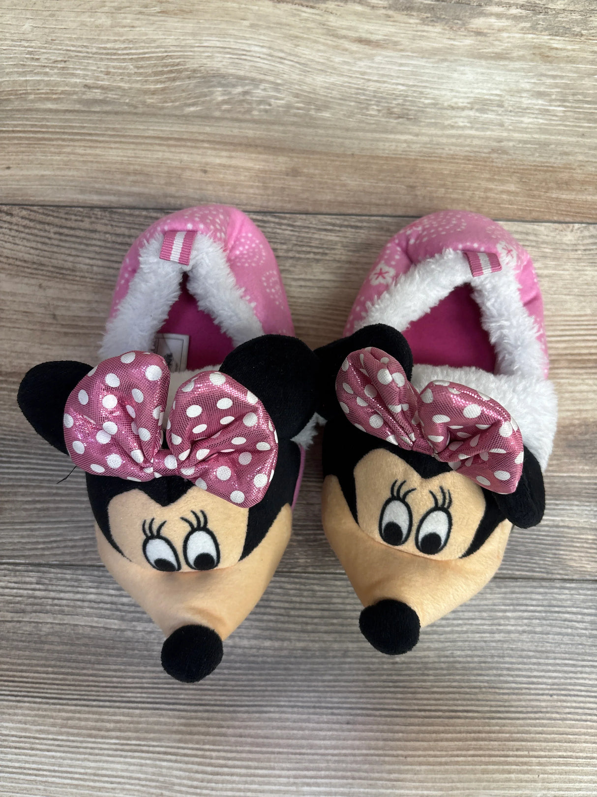 Pair of pink children's slippers with Minnie Mouse faces and polka dot bows on wooden floor