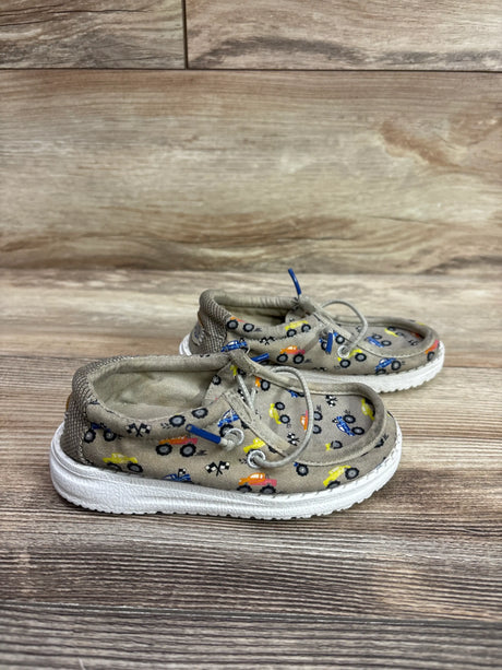 Side view of Hey Dude Wally T Trucks shoes showcasing tan fabric, colorful vehicle prints, laces, and white soles on a wood surface