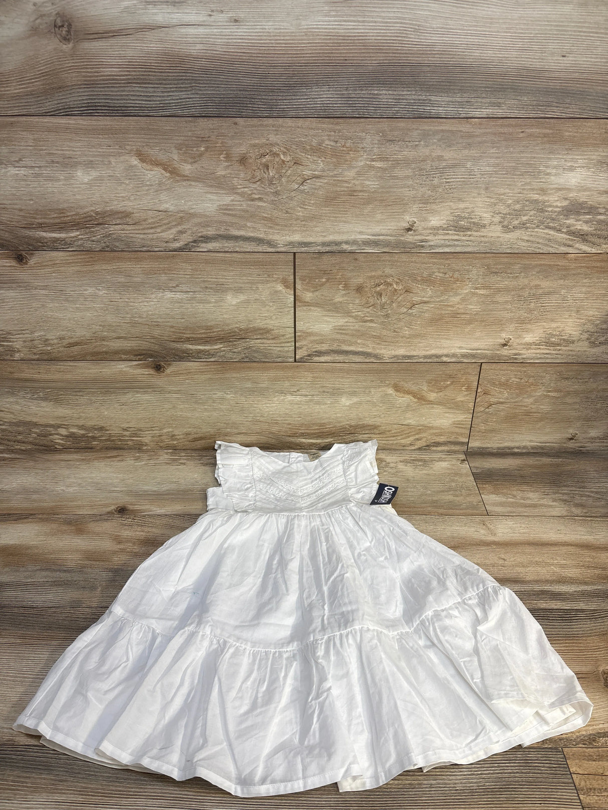 White tiered girls dress with ruffle sleeves displayed on wood floor
