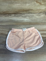 Flat lay of pink toddler shorts with white piping and small front bow, elastic waistband visible, on wood background