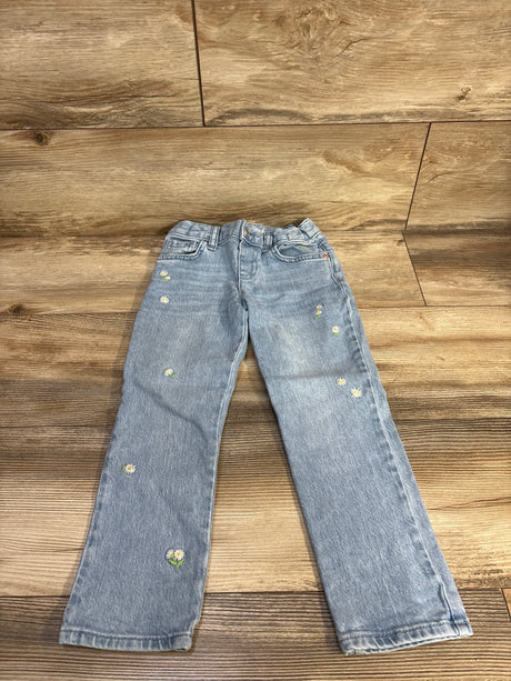 Front view of light blue toddler jeans size 5T showing embroidered white daisy motifs scattered on the legs on a wood floor background