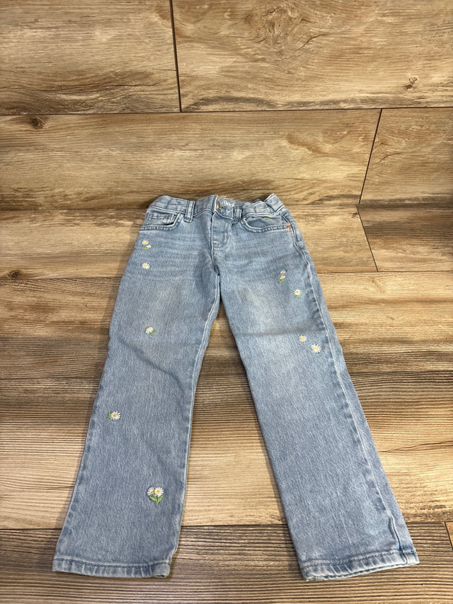 Front view of light blue toddler jeans size 5T showing embroidered white daisy motifs scattered on the legs on a wood floor background