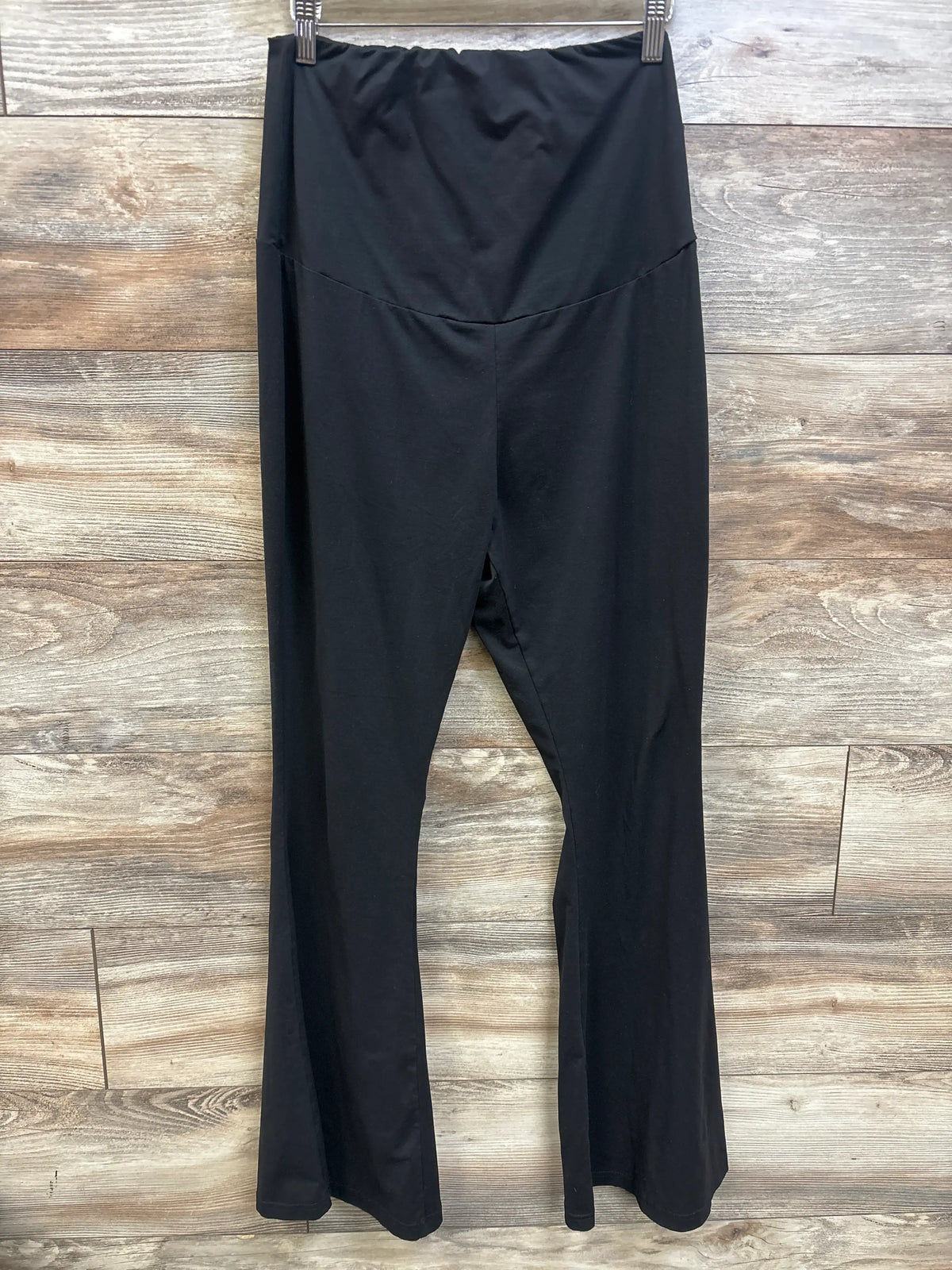 Front view of black maternity flared leggings in size Large, showcasing an over-belly waistband and flared legs on a wood background