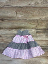 Flat-lay of toddler seersucker gingham dress in black-and-white and pink with ribbon flower at waist on wood floor, size 18M