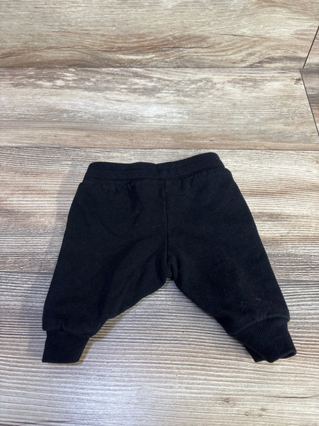Flat lay of newborn black H and M drawstring joggers showing elastic waistband and ribbed ankle cuffs on wood floor background