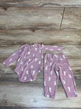 Pink baby onesie and pants set with white bunny print, soft ribbed fabric, laid on wood floor