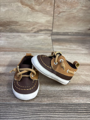 Three-quarter view of Sperry baby boat crib shoes, brown and tan upper, white sole, moc-toe stitching on wood background