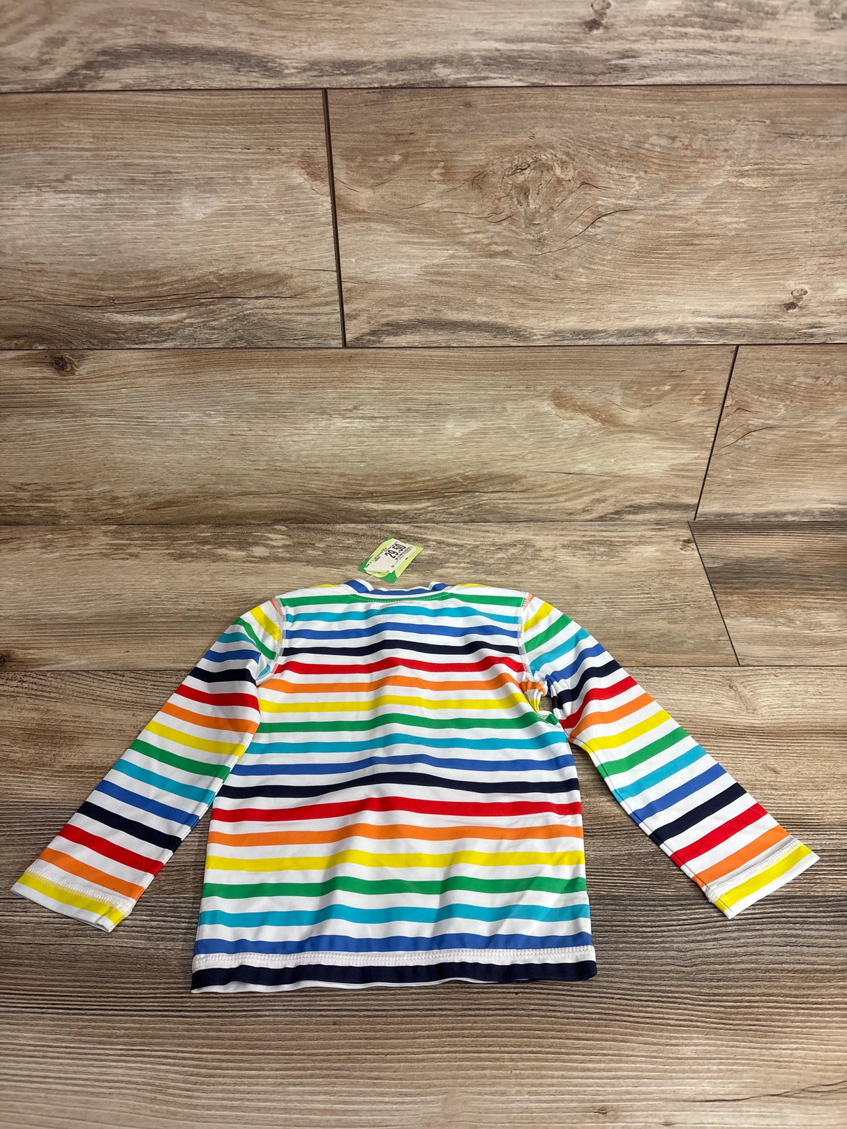Back view of baby rash guard with rainbow horizontal stripes and long sleeves on light wood floor
