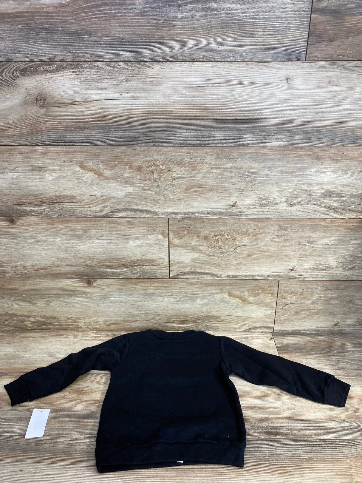 Black long sleeve kids sweatshirt laid flat on wood floor background