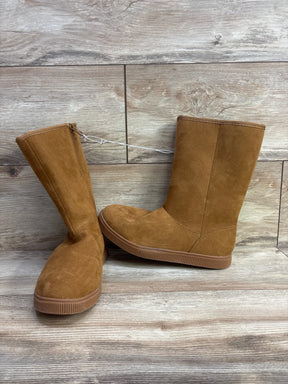 Pair of tan suede kids boots with flat soles on wood floor background