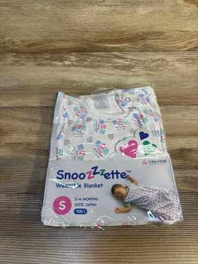 Front view of NEW Cribs For Kids Snoozzzette Wearable Blanket in white size 0-6m showcasing sealed packaging with safe sleep print labels on wood plank floor