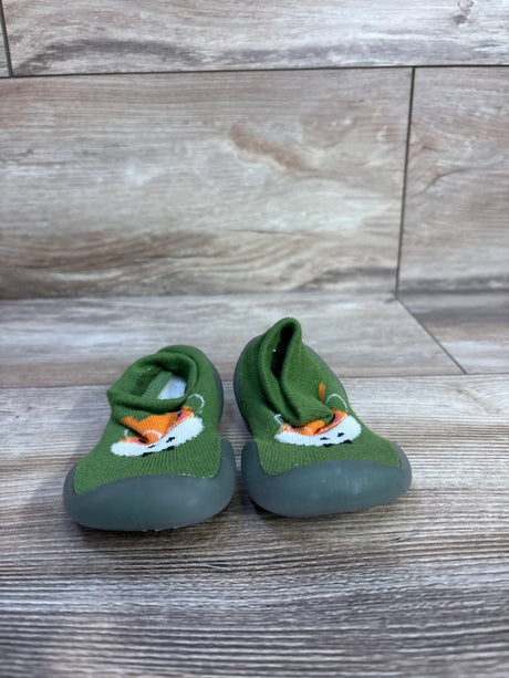 Front view of green Ikevan giraffe knitted baby sock shoes with embroidered giraffe faces and gray soles on wood floor