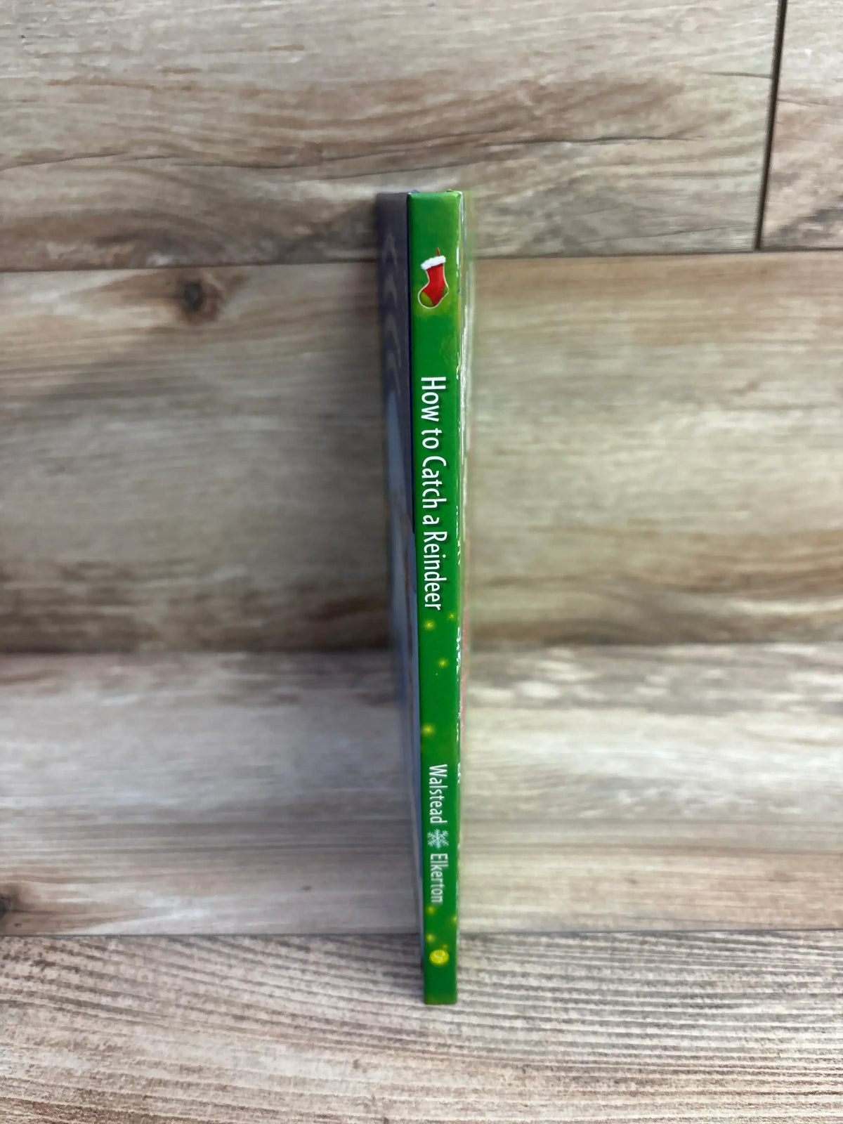 How to Catch a Reindeer children's book with green spine and stocking icon on wood background