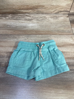 Flat lay of teal Carter's baby shorts showing elastic waistband with drawstring and front pockets on wood floor background
