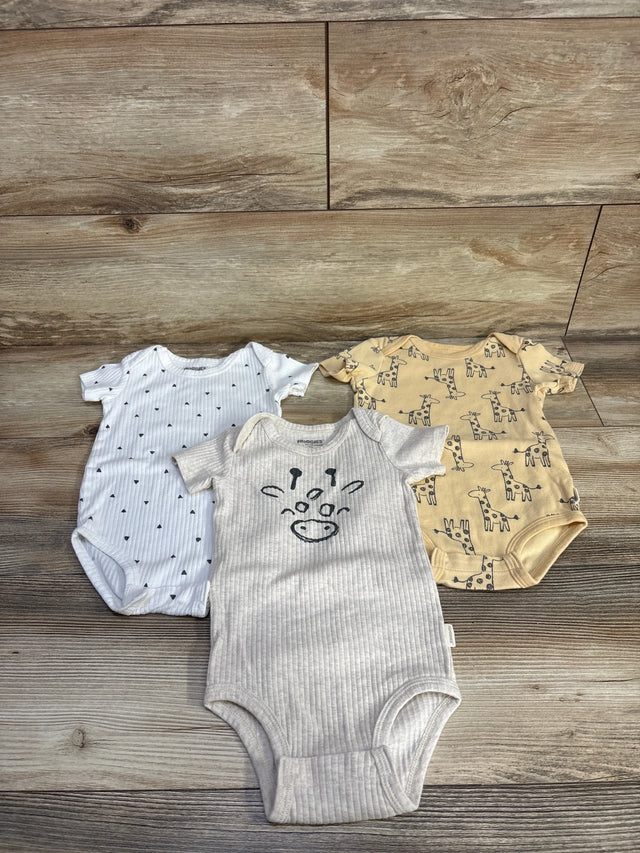 Top-down view of three baby bodysuits: beige giraffe print, cream ribbed with giraffe face, and white dotted suit on wood floor