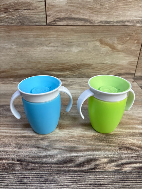 Front view of Munchkin Miracle 360 trainer cups two-pack in blue and green showcasing white handles and 360 degree spill-proof rim on wood background