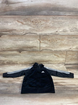 Front view of black Adidas toddler full-zip track jacket showing white three stripes on sleeves, chest logo, zip pockets on wood background