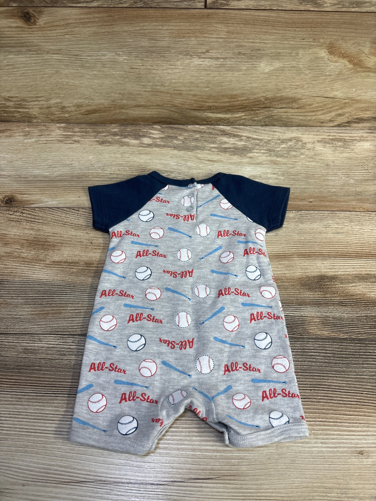 Front view of gray Little Beginnings All Star Shortie Romper with navy sleeves, baseball and bat print, snap closures, on wood