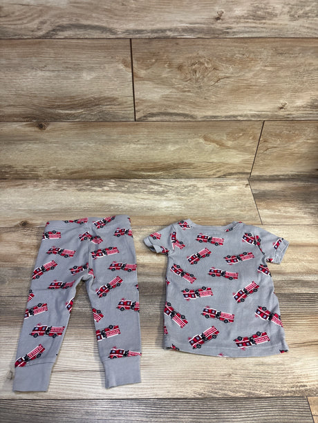 Flat lay of toddler 2-piece grey pajama set with red fire truck print on wood floor background