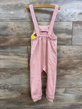 Front view of pink waffle-knit overalls with adjustable straps and elastic back on wooden hanger against wood background
