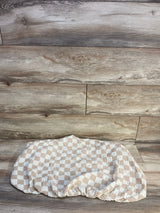 Flat lay of Brixton Phoenix muslin bassinet sheet showcasing checker pattern and elastic fitted edge on wood background