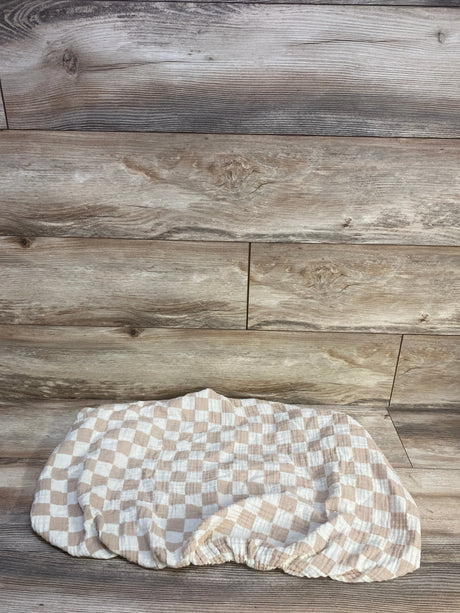Flat lay of Brixton Phoenix muslin bassinet sheet showcasing checker pattern and elastic fitted edge on wood background