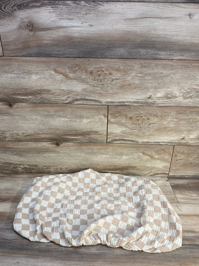 Flat lay of Brixton Phoenix muslin bassinet sheet showcasing checker pattern and elastic fitted edge on wood background