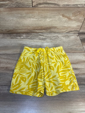 Yellow toddler shorts with leaf print pattern and drawstring waistband on wood background