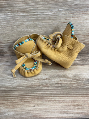 Front view of yellow leather baby moccasins showcasing hand-beaded multicolor trim and tied leather laces on wood background