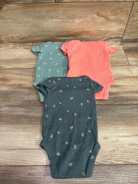 Top-down view of Just One You 3-pack baby bodysuits showcasing green floral, coral, and charcoal floral designs on wood