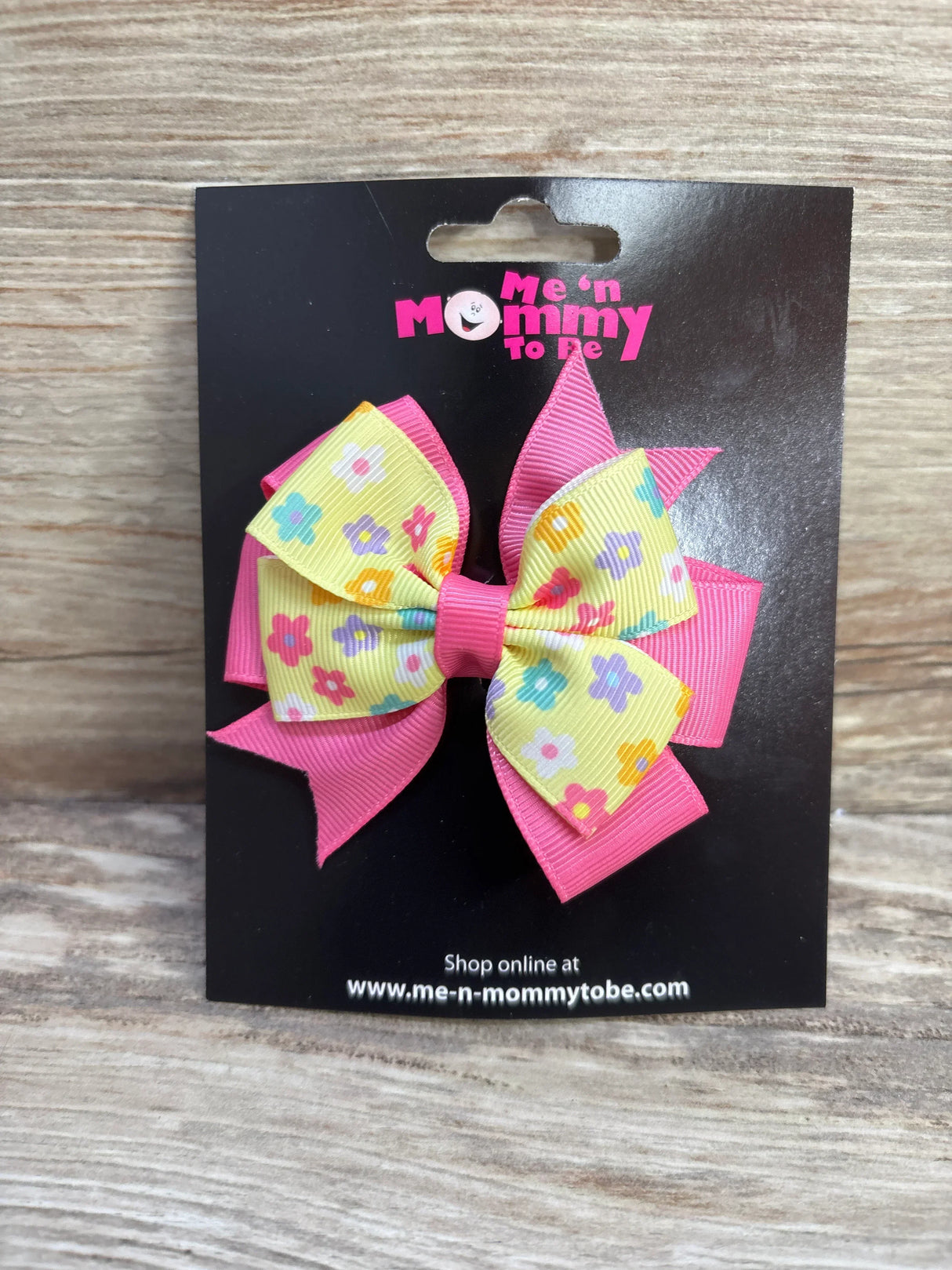 Front view of double-layer floral hair bow showing yellow flower-patterned top layer and bright pink grosgrain bottom layer on black display card